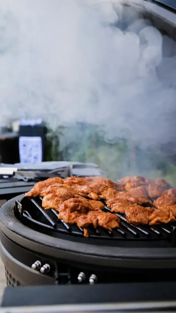 Bucăți de carne marinată pe grila unui grătar, în fum