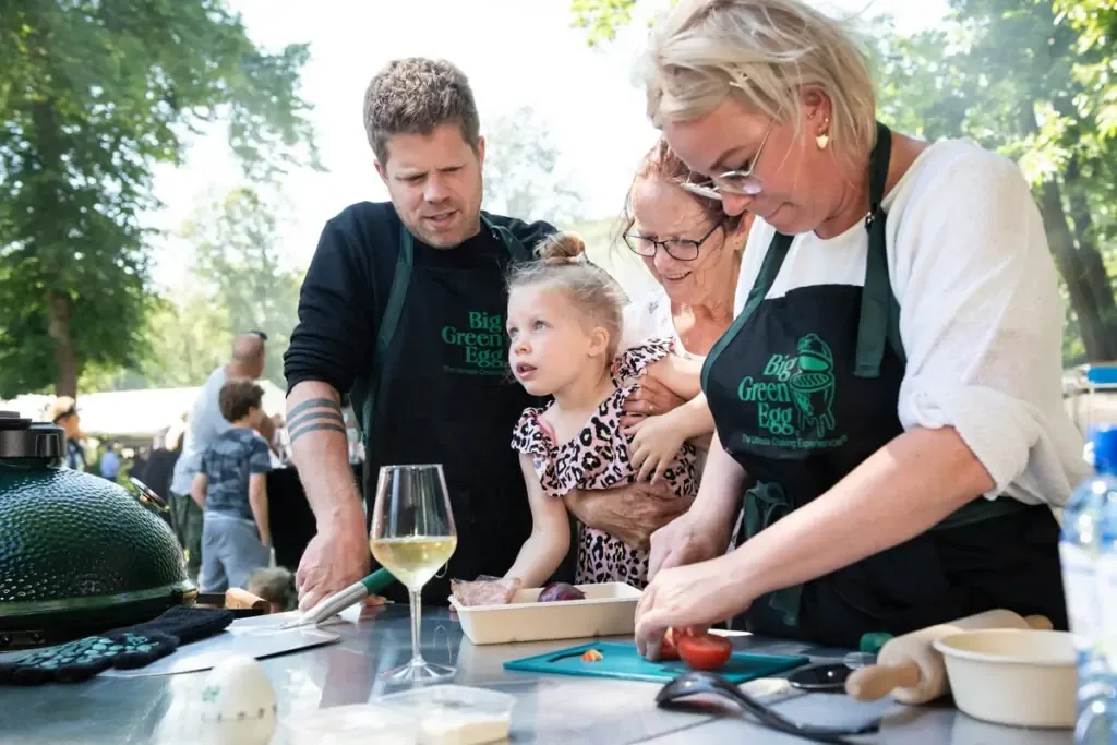 Familie care pregătește ingrediente la o masă de lucru, lângă un Big Green Egg