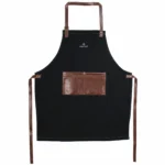 Șorț BBQ de bucătărie sau grătar manufacturat de o afacere de familie, din material denim calitativ negru și piele ecologică maro.