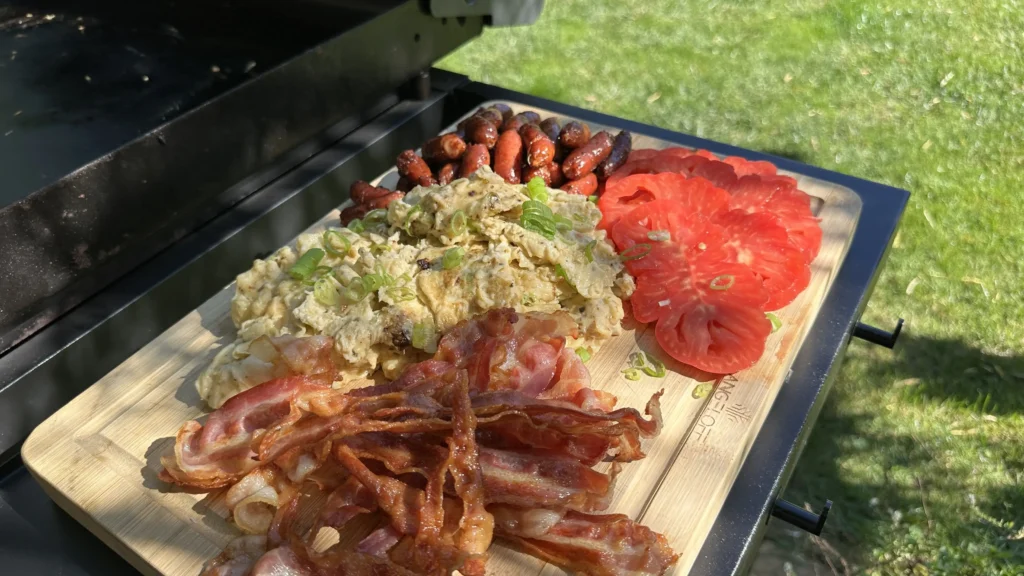 Scoate pe un tocător omleta, baconul, cârnăciorii, taie niște roșii&hellip;